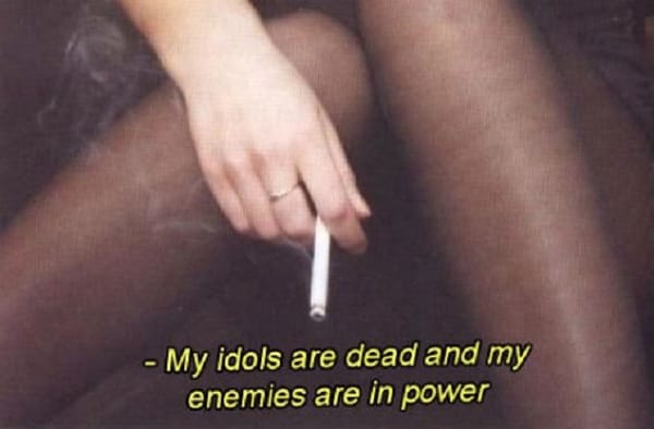 En hand som håller en cigarett, med texten: My idols are dead and my enemies are in power.